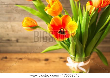 Beautiful orange tulips in a vase on a brown wooden background. Spring breath. An ideally spring mood for lovely ladies. Orange tulips are wonderful.