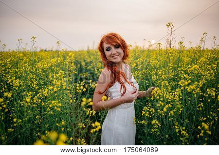 Young beautiful red-haired woman in a blooming rapeseed field at sunset