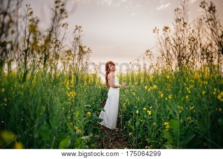 Young beautiful red-haired woman in a blooming rapeseed field at sunset