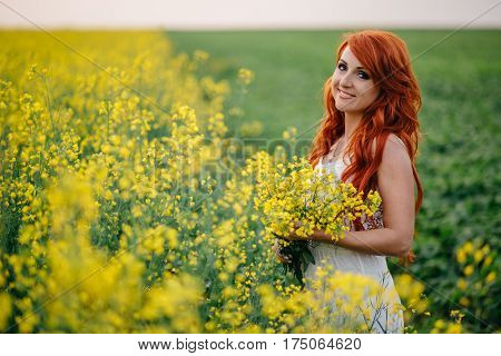 Young beautiful red-haired woman in a blooming rapeseed field at sunset