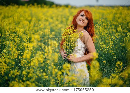 Young beautiful red-haired woman in a blooming rapeseed field at sunset