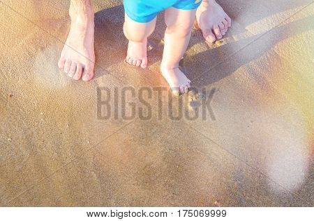 Toddler baby doing his first steps on the beach. Bare feet father and son staying on the sand near the bank in sunny day. Summertime holidays concept. Top view. Copy space.