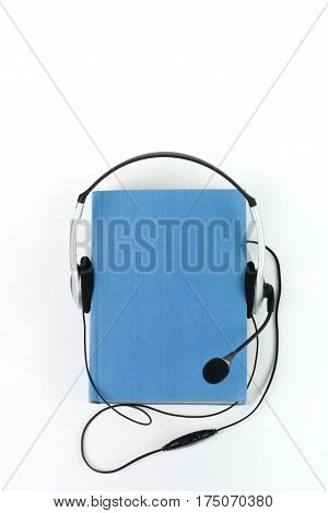 Audiobook on white background. Headphones put over blue hardback book empty cover copy space for ad text. Distance education e-learning concept