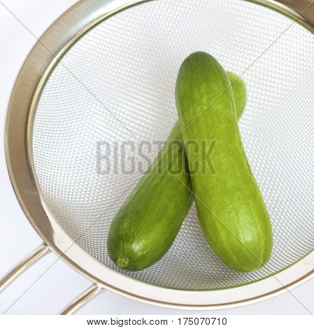 Two green cucumbers in a kitchen sieve.