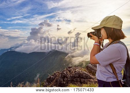 Hiker asian teens girl with digital camera and backpack taking photo beautiful landscape natural of sierra and sky during sunset on mountain at Phu Chi Fa Forest Park Chiang Rai Thailand