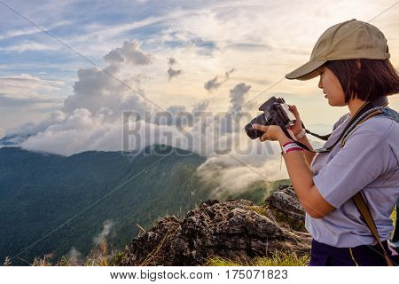 Hiker asian teens girl wear caps looking photo on digital camera is beautiful landscape natural of sierra and sky during sunset on mountain at Phu Chi Fa Forest Park Chiang Rai Thailand