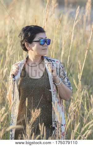 portrait of asian woman wearing sun glasses standing with relaxing post in beautiful grass field