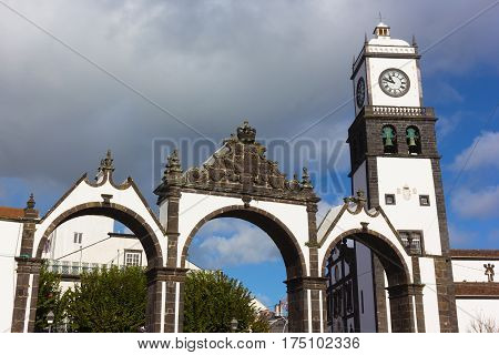 Portas da Cidade Gates and Saint Sabastian church with clock tower Ponta Delgada Portugal. Azores capital landmarks under cloudy skies.