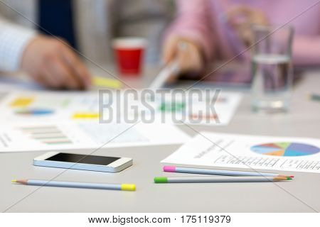 Solving Business Issue Concept - grey Office Table with Color professional Charts on Papers Pencils and Electronic Gadgets blurred Body of Businesspeople on Background