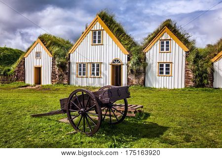 The concept of the historical and cultural tourism. Interesting ethnographic museum Glaumbaer in Iceland. Facade of the farmhouse, covered with grass, and ancient rural two-wheeled wheelbarrow