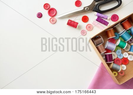 needlework, craft, sewing and tailoring concept - box with thread spools and buttons on table