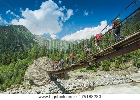 Group of hikers with backpacks go on a suspension bridge over the mountain river. Caucasian mountains Georgia Svaneti region.