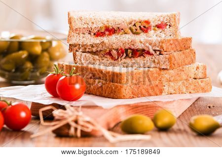 Tuna olives and tomato sandwiches on wooden table.
