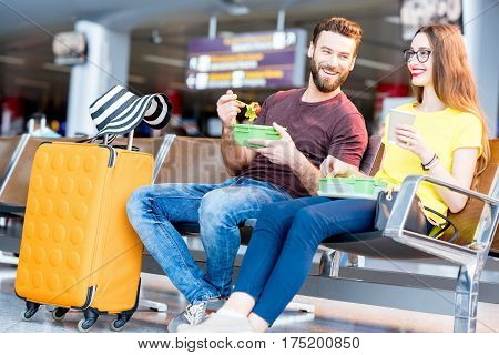 Young couple having a snack with lunch boxes at the waiting hall of the airport during their vacation