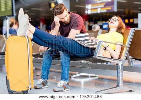 Young couple sleeping on the chairs at the waiting room of the airport. Long waiting for the airplane