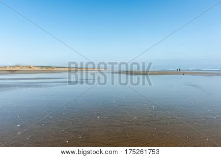 Small distant figures of couple walking along on wide flat sand by the sea at Ninety Mile beach Northland New Zealand