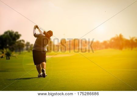 female golf player swinging golf on fairway during sunset with flare