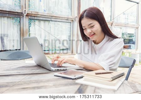 happy smiling young casual asian woman using technology on her laptop computer outdoor in her garden with computer tablet and notebooks on the table