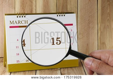 Magnifying glass in hand on calendar you can look Fifteenth day of monthFocus number fifteen in MarchConcept in business and meetings.