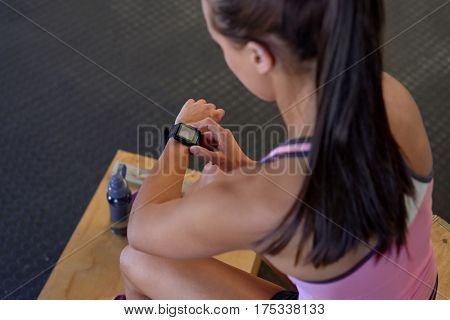 Sporty woman sitting and checking smart watch fitness activity tracker monitor isolated in gym before exercise