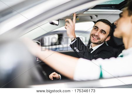 Let me show you interior of this car. Handsome young classic car salesman standing in the dealership and helping a client to make a decision about car