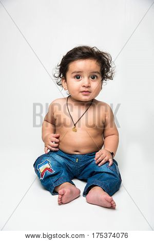 Indian Cute naked baby boy in blue denims or jeans smiling and sitting over white background