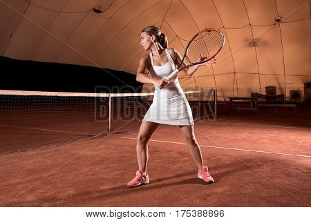 Sportswoman at the tennis court with racquet. Indoor tennis court