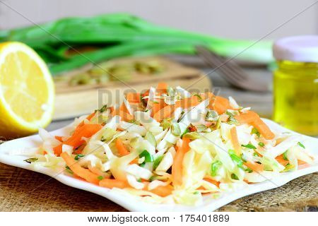 Simple coleslaw salad. Coleslaw salad with fresh carrots, green onion and pumpkin seeds on a plate. Salad ingredients on a wooden table. Healthy vegetable food. Closeup