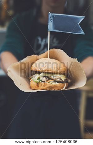 Fresh burger cooked at barbecue outdoors. Cookout american bbq with text flag. Big hamburger with steak meat and vegetables closeup with chef unfocused at background. Street fast food.