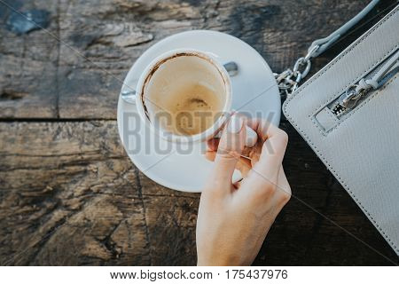 Female hand with an empty cup of coffee on the vintage wooden table. Female beautiful bag.