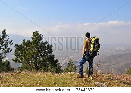 Young man with backpack standing on top of the hill over the city