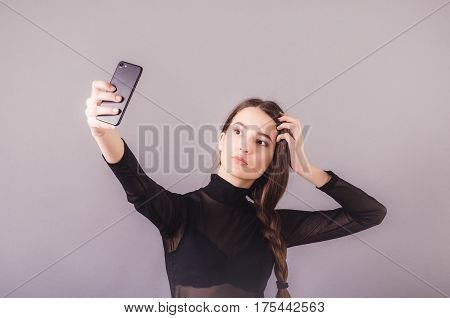 Portrait of a young attractive girl making selfie photo with smartphone isolated on a neutral gray background
