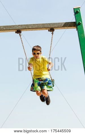 Rest and relax for children. Little boy in sunglasses resting swinging outdoor. Adorable child having fun playing in playground.
