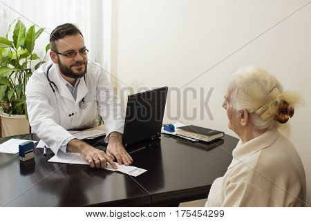 geriatrician doctor with a patient in his office.A doctor at work. He shows a finger and translates the patient record on the prescription.