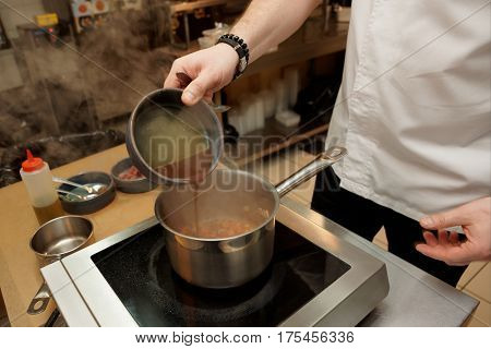 Restaurant chef is cooking soup in commercial kitchen, adding demiglaze