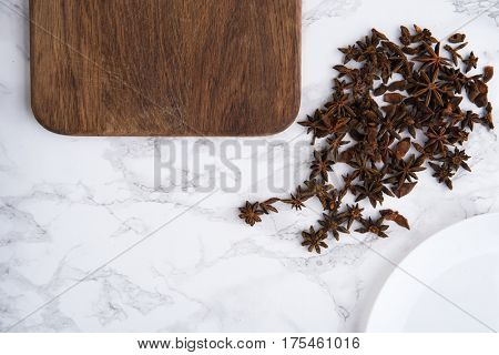 Close up portrait of anise seeds and wooden cutting board on white marble background
