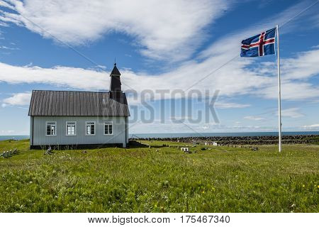 Strandkirkja on Iceland with Icelandic flag green meadow and ocean.