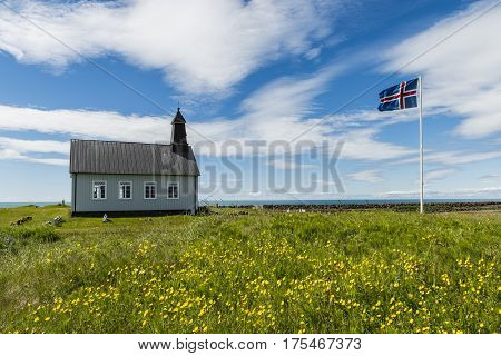 Strandkirkja on Iceland with Icelandic flag green meadow yellow buttercups and ocean.