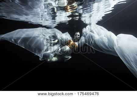 Pregnant woman swimming underwater in front of black background