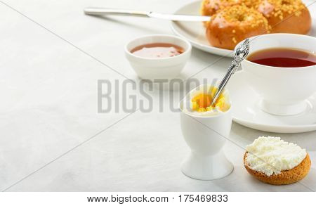 Delicious and healthy breakfast of boiled egg and brioche buns with black tea on a light background. Copy space soft focus.