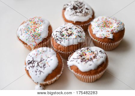 White authentic cupcakes made by hands with multicolored powder lying on white table