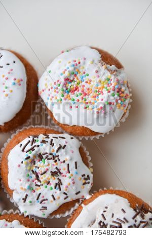 White authentic cupcakes made by hands with multicolored powder lying on white table