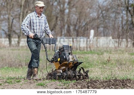 Man working in the garden with garden tiller. Garden tiller to work. Man with tractor cultivating field at spring. Farmer loosens soil by petrol cultivator