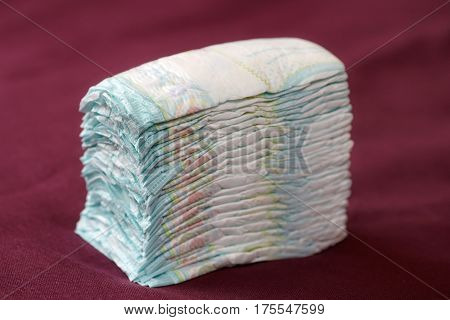Stack of diapers or nappies on purple background closeup