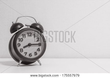 Closeup alarm clock for decorate show a quarter past eight o'clock or 8:15 a.m.on white wood desk and cream wallpaper textured background in black and white tone with copy space