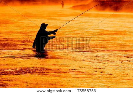 Man flyfishing in misty river in the morning light