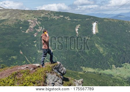 DZEMBRONYA UKRAINE - JUNE 16 2016: A young man stands on the cliff of a mountains and speaks via smartphone.