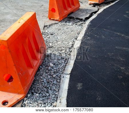 Road construction. New asphalt concrete concrete curb and orange safety barriers on the road.