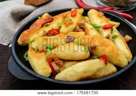 Popular traditional Czech Hungarian German dish: potato knedli (dumplings) with slices of fried bacon spicy red pepper and green onions. Serving on a cast iron pan.