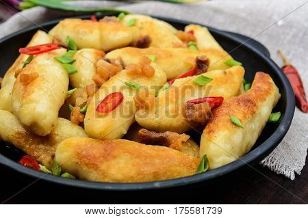 Popular traditional Czech Hungarian German dish: potato knedli (dumplings) with slices of fried bacon spicy red pepper and green onions. Serving on a cast iron pan.